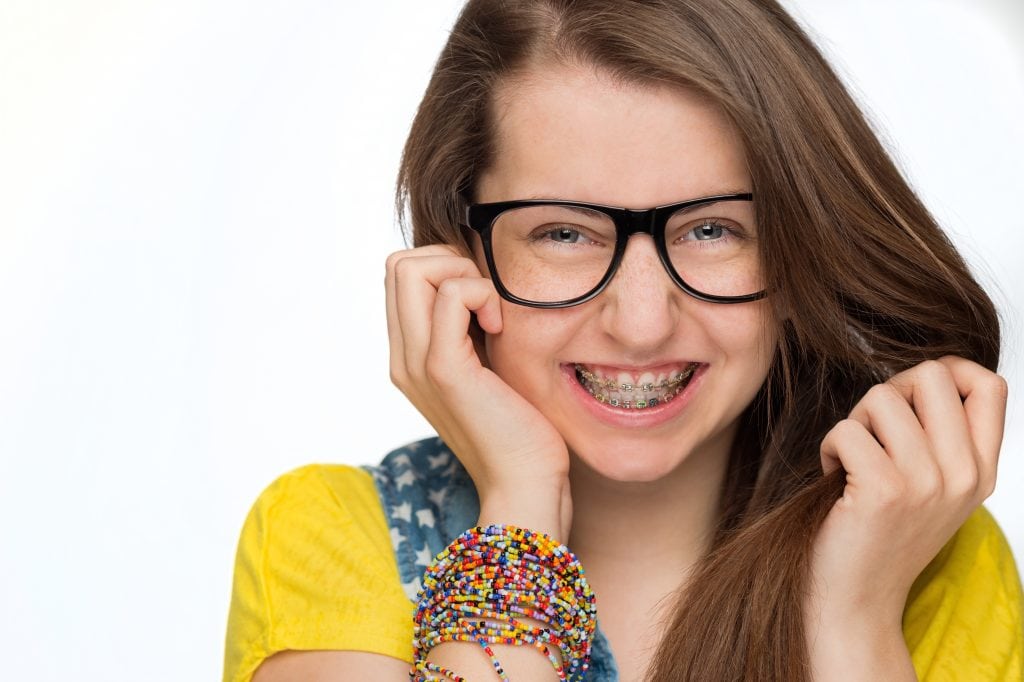 Cheerful girl with braces wearing geek glasses on white background